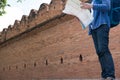 young traveler reading map. asian man wearing blue shirt and jeans standing near old orange brick wall with backpack Royalty Free Stock Photo