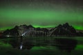 Young traveler standin in front of Vestrahorn Stockknes mountain range with aurora borealis and reflection at the beach Royalty Free Stock Photo