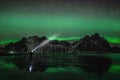 Young traveler standin in front of Vestrahorn Stockknes mountain range with aurora borealis and reflection at the beach