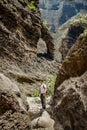 Young traveler stays on the top of huge boulder in the Masca gorge, Tenerife, showing solidified volcanic lava flow layers and