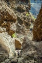 Young traveler stays on the top of huge boulder in the Masca gorge, Tenerife, showing solidified volcanic lava flow layers and