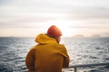 Young traveler wearing red hat and yellow raincoat floating on ship looking at sunset sea after storm and foggy mountains on skyli Royalty Free Stock Photo