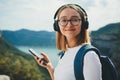 Young traveler woman with hipser glasses and backpack holds cellphone device in hands and selects music for headphones Royalty Free Stock Photo