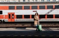 Young traveler woman with luggage waiting for train at train station platform.Train in the background. Royalty Free Stock Photo