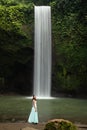 Young traveler woman at waterfall in tropical forest, Ubud, Bali. Tibumana waterfall. Slow shutter speed, motion photography Royalty Free Stock Photo