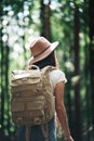 Young traveler woman wearing traveling backpack and hat walking among trees in forest on outdoors Royalty Free Stock Photo
