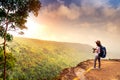 Young traveling woman with backpack hat and camera stand on the top of the mountain cliff watching beautiful view of woods and sky