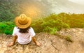 Young traveling woman wearing hat and sitting on the top of the mountain cliff with relaxing mood and watching beautiful view