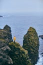 Young traveller in yellow jacket standing on the cliff in Iceland or norway in cold season and enjoying sea landscape