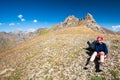 Young trekker woman resting in rocky pass with mountain top wiews in high mountains. Woman with sunglasses sitting next to