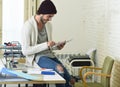 Young trendy businessman in beanie and cool hipster informal look sitting on home office desk using digital tablet pad happy Royalty Free Stock Photo