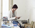 Young trendy businessman in beanie and cool hipster informal look sitting on home office desk using digital tablet pad happy Royalty Free Stock Photo