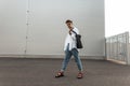 Young trendy young man walks on the city on a summer day. Handsome urban guy in fashionable white and denim clothes in red shoes Royalty Free Stock Photo