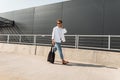 Young trendy young man walks on the city on a sunny day. Handsome hipster guy in fashionable clothes in summer shoes with a bag Royalty Free Stock Photo