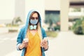 Young trendy woman influencer using mobile phone on city street while wearing protective face mask Royalty Free Stock Photo