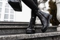 Young trendy woman in stylish leather black boots in jeans with a bag stands on the stone steps in the city. Close up of female Royalty Free Stock Photo
