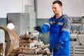 Young turner in overalls works on lathe in workshop. Authentic scene workflow. Caucasian worker recycles metal parts