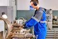 Young turner in safety glasses and headphones works at lathe in workshop. Authentic scene workflow. Caucasian worker