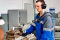 Young turner in safety glasses and headphones works at lathe in workshop. Authentic scene workflow. Caucasian worker