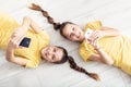 Young twin girls lying on the floor, both holding mobile phones in their hands Royalty Free Stock Photo