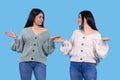 Young twin sisters, two women wearing casual clothing: sweater and jeans over isolated blue background holding copyspace