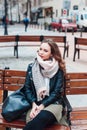 young curly stylish woman wearing black jacket sitting on a bench in city