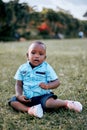 Young Ugandan baby boy in a blue shirt sitting on the grass.