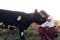 Young Ukrainian woman sits, smiles and holds calf dressed in traditional national clothes on pasture