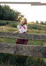 Young Ukrainian woman stands in traditional national clothes near wooden fence on meadow at sunset Royalty Free Stock Photo