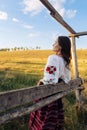 Young Ukrainian woman stands in traditional national embroidered shirt and skirt near wooden fence on meadow Royalty Free Stock Photo