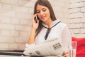 Woman reading a newspaper and talking on mobile phone Royalty Free Stock Photo