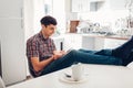 Young unemployed man hanging in phone after dinner with his legs raised on kitchen table. Social network addiction Royalty Free Stock Photo