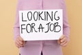 Young unemployed woman holding sign with phrase Looking For A Job on beige background, closeup Royalty Free Stock Photo