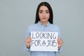 Young unemployed woman holding sign with phrase Looking For A Job on grey background Royalty Free Stock Photo