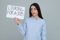 Young unemployed woman holding sign with phrase Looking For A Job on grey background Royalty Free Stock Photo