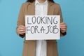 Young unemployed woman holding sign with phrase Looking For A Job on light blue background, closeup Royalty Free Stock Photo