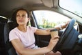 Young unfastened woman driver looking to the side while driving a car and drinking coffee from a takeaway cup Royalty Free Stock Photo