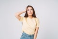 Young unhappy asian woman with long hair in yellow shirt and jeans holding her hands on head on grey background Royalty Free Stock Photo