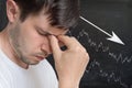 Young unhappy and disappointed man and chart with arrow down on blackboard in background