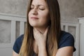 Young unhappy woman has sore throat. The girl feels pain, symptoms of the beginning of a cold, flu or virus. Tired girl sitting at Royalty Free Stock Photo