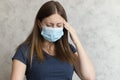 Young unhappy woman in medical face mask has headache. The girl feels pain, symptoms of the beginning of a cold, flu or virus. Royalty Free Stock Photo