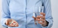 Young unknown woman holding pills and glass of water, closeup of hands. Medicine and healthcare concept Royalty Free Stock Photo