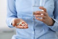 Young unknown woman holding pills and glass of water, closeup of hands. Medicine and healthcare concept Royalty Free Stock Photo