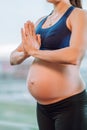 Young unrecognisable pregnant woman in sportswear stay and meditate and practice yoga on window background.