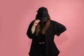 Young unrecognizable woman in black baseball cap lowered head down. Mock-up, copy space. Sportswear, pink background, studio shot