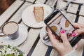 Young unrecognizable woman taking a picture with mobile phone of her breakfast, a cup of coffee and a piece of cake. Breakfast Royalty Free Stock Photo