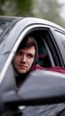 Young unshaven man in red jacket with black hood sitting at wheel of a car Royalty Free Stock Photo