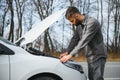 Young upset casual man trying to fix his broken car outdoors. Man waiting for towing service for help car accident on Royalty Free Stock Photo