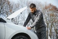 Young upset casual man trying to fix his broken car outdoors. Man waiting for towing service for help car accident on Royalty Free Stock Photo