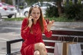 Young upset Caucasian woman in red dress sitting on a bench talking on the phone to clear up a charge on her credit card